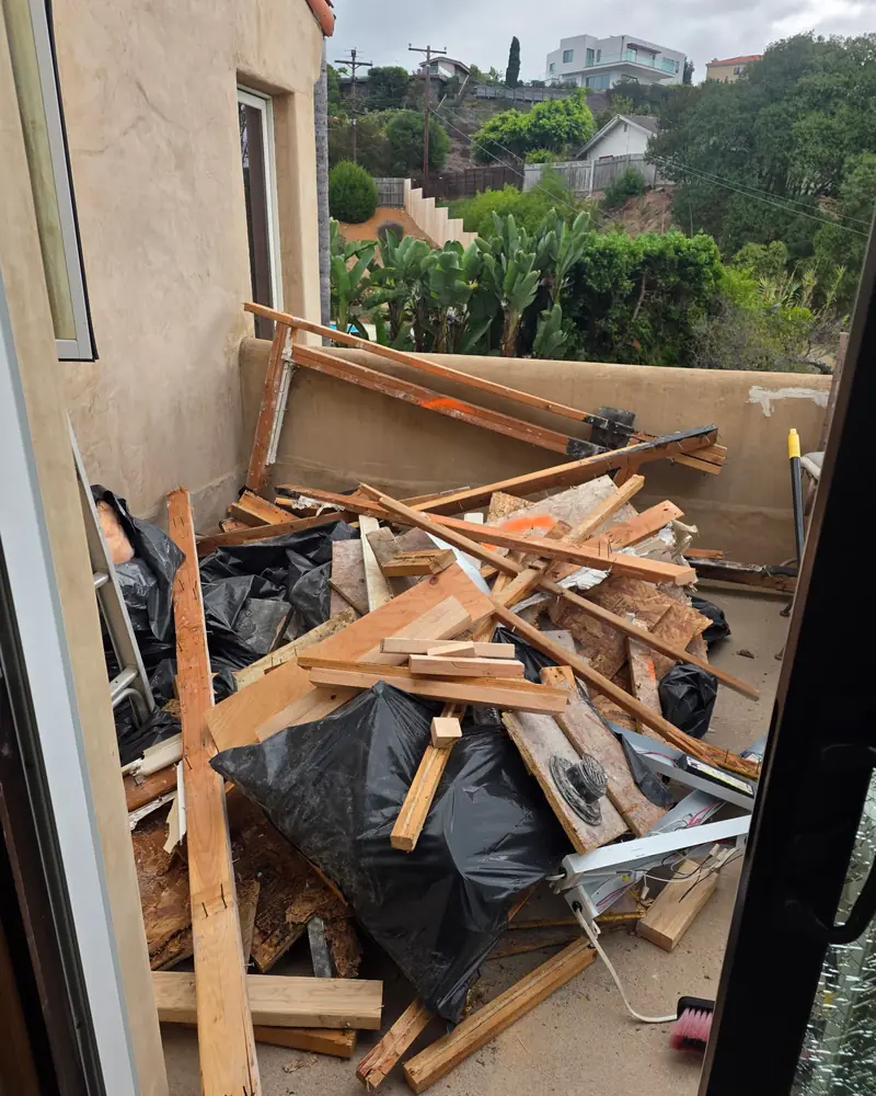 Before: balcony in San Diego County piled with broken lumber, boards and black bags of debris