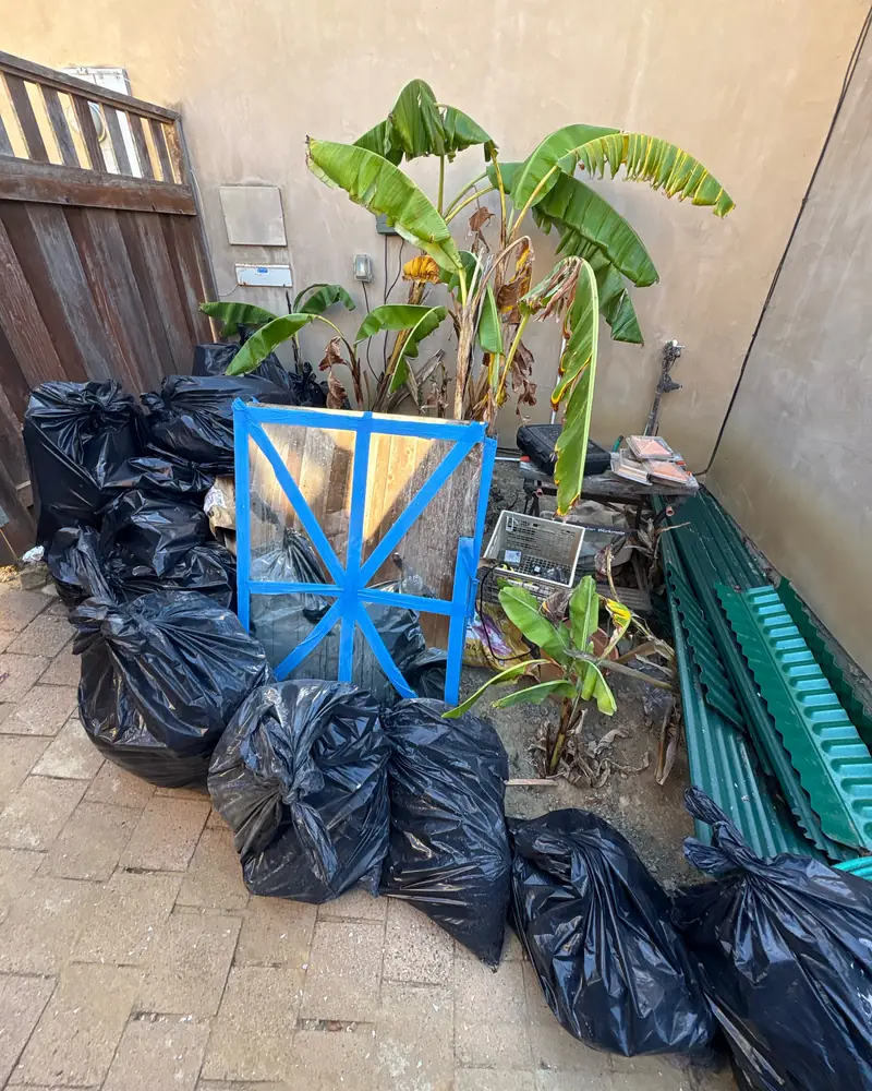 Black contractor bags of yard waste and leftover panels stacked on a patio, waiting to be hauled away